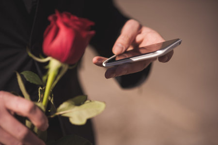 men holds red rose while calling on mobile phone