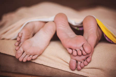 couple barefoot in bed under blanket no faceの写真素材
