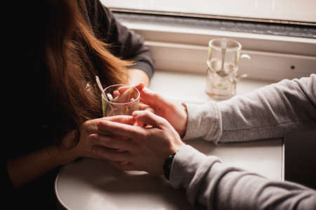couple hands wrapped around a glass cup in trainの写真素材