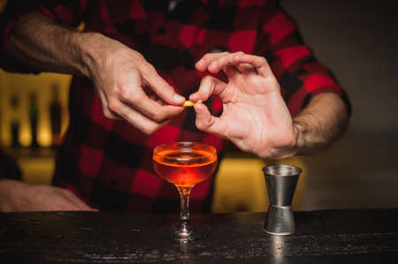 male bartender is squeezing orange peel into a cocktail glassの写真素材
