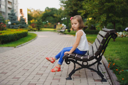 sad little girl sitting on the bench in the park at the day timeの写真素材