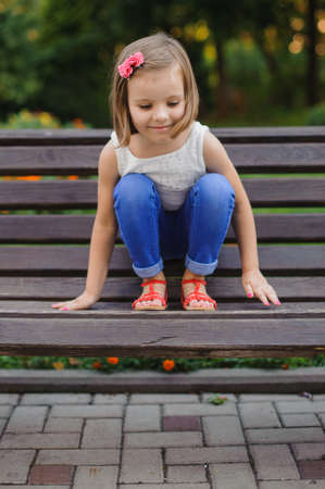 Little cute girl sits with feet on benchの写真素材