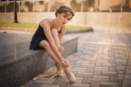 Slim young ballerina in a blackdress putting on pointe shoes. outdoorの写真素材