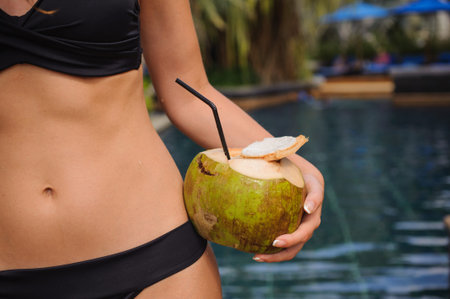 Young woman holding coconut with straw near pool