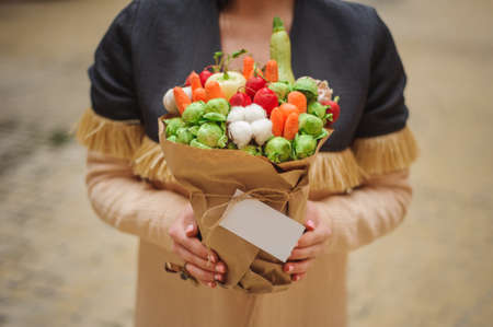 The original unusual edible bouquet of vegetables and fruits in woman hands  with cardの写真素材