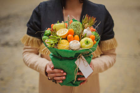 The original unusual edible bouquet of vegetables and fruits in woman hands  with cardの写真素材