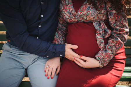 men holds hands on belly of pregrant women in red dress no face