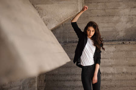 Young brunet woman standing outside in black jacket, jeans wearing hills  looking in camera . horizontalの写真素材
