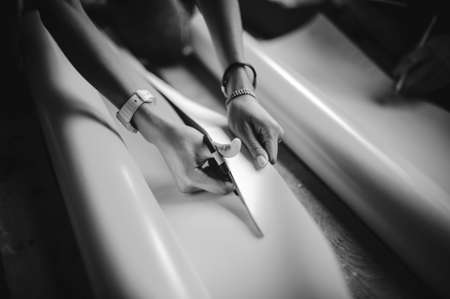 Female hand holding blue scissors cutting white paper black and whiteの写真素材