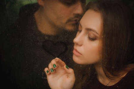 shot through the window young couple in love drawing heart on glassの写真素材