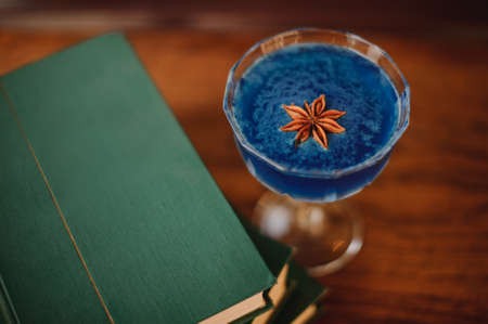Blue cocktail with Star Anise on bar next to booksの写真素材