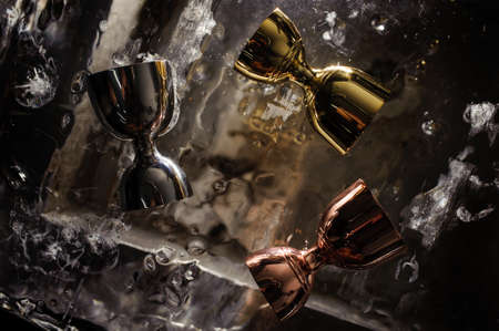 three shiny stainless steel jiggers for alcoholic beverage on a solid iceの写真素材