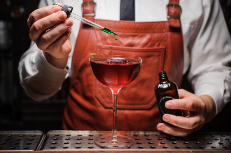 Expert barman is making cocktail and finishing up by dropping green bitter