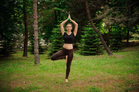 Practicing yoga with trees Attractive young caucasian woman standing in yoga tree pose on the grass.の写真素材