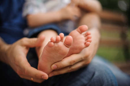 Little baby feet in daddy's hands on nature outdoors. summer park on background.の写真素材