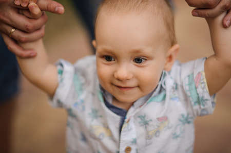 Baby boy learning to walk and making his first steps holding the hands of his father.の写真素材
