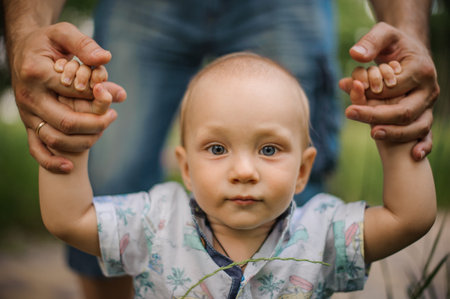 Baby boy learning to walk and making his first steps holding the hands of his father.