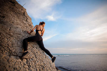 Female rock climber watching sunset over the seaの写真素材
