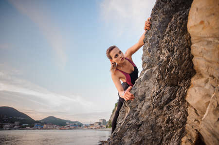 Portrait of young female rock climber overhanging a rock cliff. Beautiful blue sky, city and mountains on the background.の写真素材
