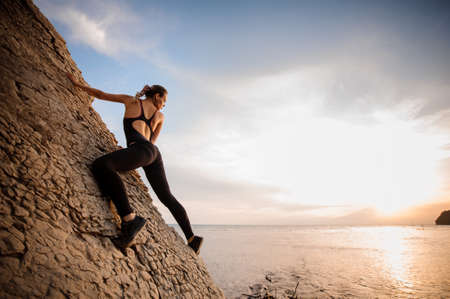 Female extreme climber conquers steep rock against the sunset over the river.の写真素材