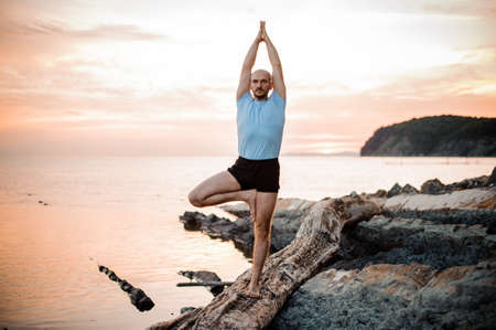 Yoga posture on sunset by man near seaの写真素材
