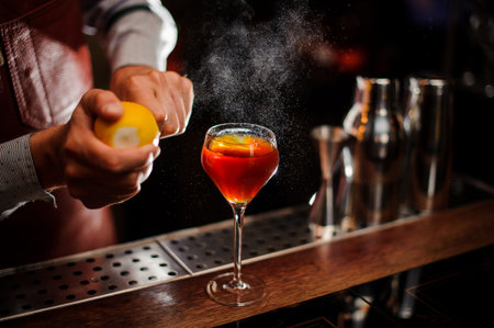 Bartender is adding lemon zest to the red cocktail at bar counter. Selective focus