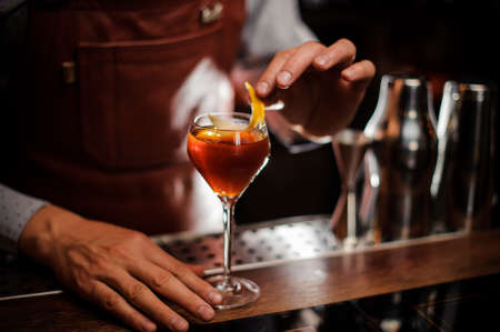 Bartender with glass and lemon peel preparing cocktail at barの写真素材