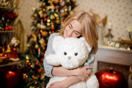 Beautiful young woman hugging a teddy bear, Christmas tree in the background. Happy New Yearの写真素材