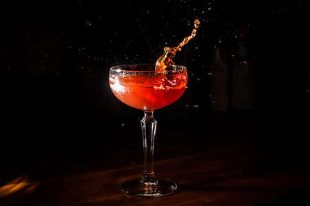 red martini cocktail splashing into glass on black and wooden backgroundの写真素材