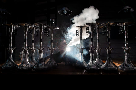 Man smokes a hookah on the dark background. The pleasure of smoking.