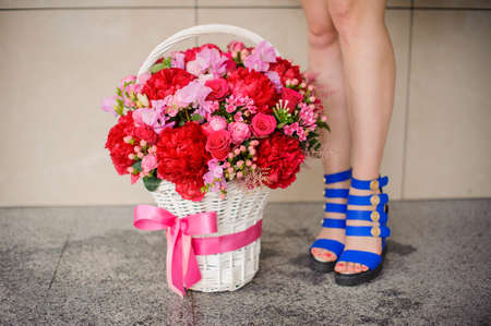 Beautiful wicker basket of colorful flowers near the girl legs on the light background no face close upの写真素材