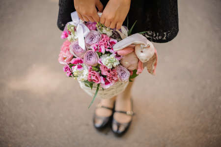 Girl holding a pretty wicker basket of colorful flowers with toy on the light background no faceの写真素材