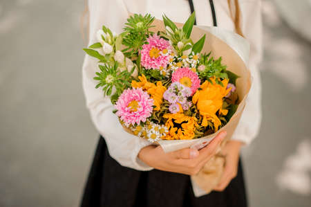Schoolgirl holding a little pretty bouquet of colorful flowers on a light background no face close upの写真素材