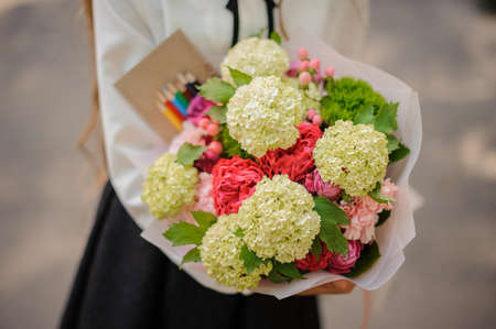 Schoolgirl holding a beautiful bouquet of colorful flowers on a light background no face close upの写真素材