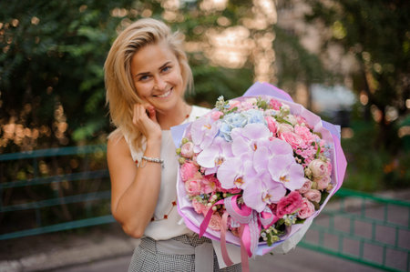 Beautiful and smiling blond girl holding a pretty and soft composition of many beautiful and colorful flowersの写真素材