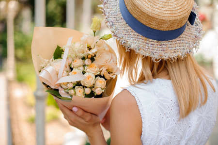 Woman in a pretty straw hat holding a little beautiful bouquet of flowers close upの写真素材