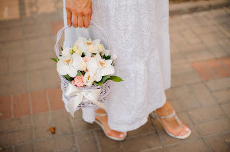 Woman in white dress holding a pretty wicker basket of flowers no face close upの写真素材