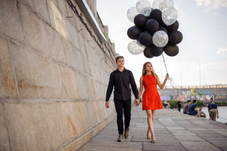 Young and beautiful couple walks along the promenade, holding hands. Girl holds black balloonsの写真素材