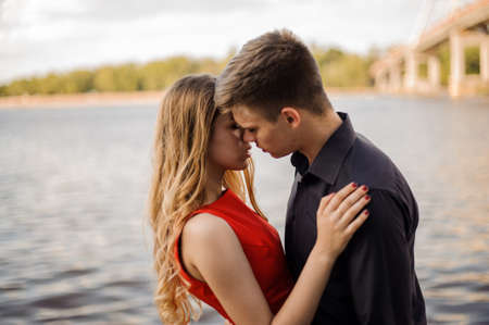 Cute and happy couple in love, hugging on the background of water. The guy tries to kiss a girlの写真素材