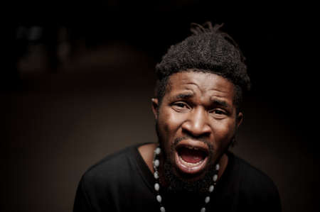 Close up emotional portrait of afro american guy with opened mouth on the dark backgroundの写真素材