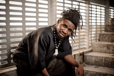 Young and attractive african american man with dreadlocks and dressed in black clothes sitting near the windowの写真素材