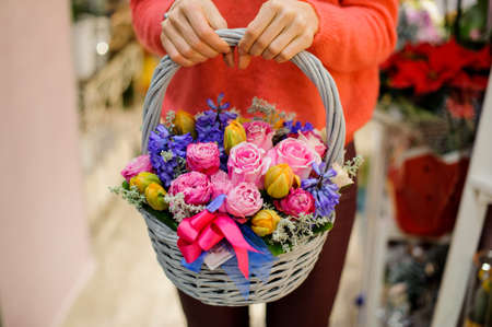 Pretty wicker basket with beautiful and colorful flower composition in woman hands. No face, close upの写真素材
