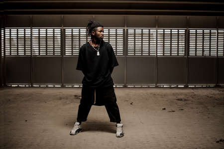 Afro american man with dreadlocks and in trendy black clothes standing with legs wide apart. Full lengthの写真素材