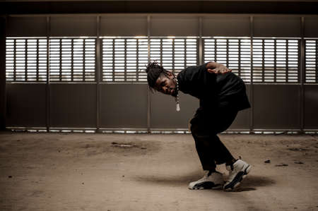 African american man with dreadlocks and in black clothes and white sport shoes in dance on the grey backgroundの写真素材