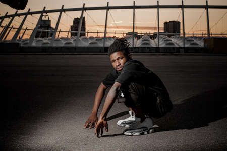 Outdoor portrait of the squatting on the ground young afro american guy dressed in black clothesの写真素材
