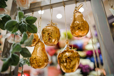 Pretty golden glass fruit-shaped Christmas tree toys hanging on the ropes on the bright backgroundの写真素材