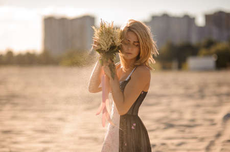 Sexy and lovely blond woman with bouquet of flowers in hands on the background of sandの写真素材