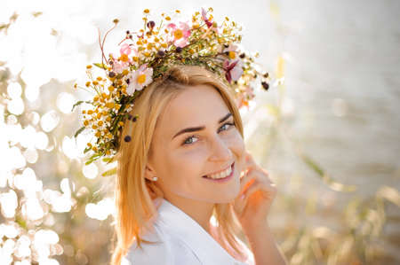 Romantic smiling blond girl in a wreath of flowers on the background of water close upの写真素材