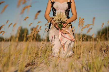 Sexy woman body in beautiful lingerie on the field. Hands holding bouquet of flowers. No faceの写真素材