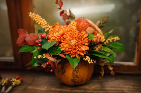 Pumpkin with beautiful and bright autumn flowers inside, standing on the brown wooden window sillの写真素材